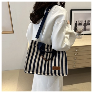 Détail du sac cabas en toile rayée montrant le profil latéral et l'étiquette en cuir