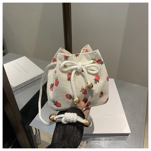 Detail of strawberry print corduroy bucket bag with drawstring and golden metal balls