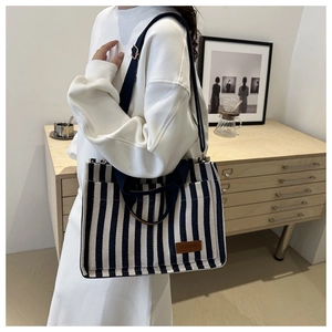 Detail of navy striped canvas tote bag showing fashion leather patch and side pocket