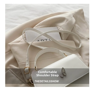Close-up of a white leather crossbody bag featuring a decorative golden butterfly clasp