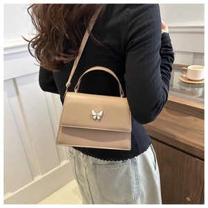 Chic beige square bag with butterfly clasp detail shown worn over the shoulder