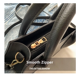 Close-up of smooth gold-tone metal zipper and textured black leather surface on handbag