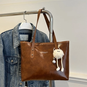 Classic brown leather tote bag with stylish white fuzzy doll pendant on blue denim jacket