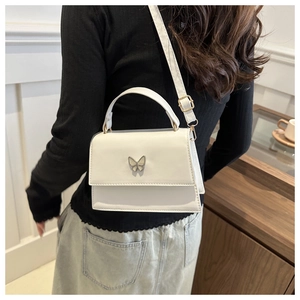 Detail of white PU leather crossbody bag featuring a silver butterfly metal ornament