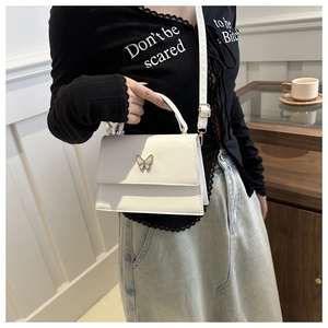 Detail shot of a white mini trapezoid bag featuring a silver butterfly clasp and PU leather