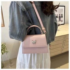 Detail of pink crossbody bag with butterfly ornament worn over a white dress