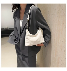Close-up of white soft leather shoulder bag with decorative pearl strap on model suit