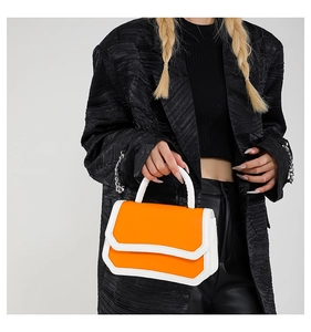 Detail of vibrant orange and white contrast handbag held by model in black suit