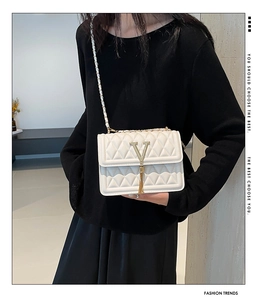 Detail of white quilted crossbody bag with gold V-shaped buckle and metal fringe tassel