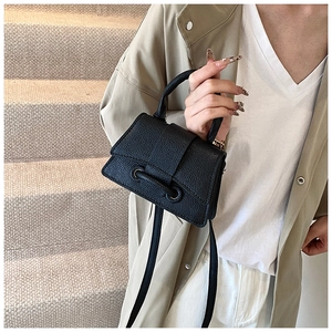 Detail of black litchi texture handbag with metallic eyelets and crossbody strap