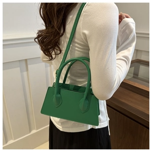 Detailed side view of an emerald green structured handbag with slim shoulder straps