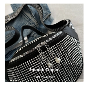 Close-up of studded crossbody bag with double zippers and pearl chain charms