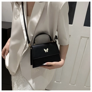 Chic black crossbody box bag with white butterfly accent and leather handle on a model
