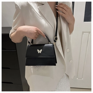 Detail of a black crossbody bag featuring a silver butterfly buckle on a white blazer