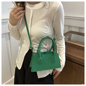 Detail of green minimalist crossbody handbag featuring textured leather and slim strap