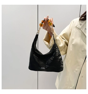 Detail of black pleated nylon tote bag with amber bead handle and classic label patch