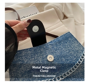 Détail de la boucle magnétique en métal et chaîne argentée sur un sac bandoulière en denim