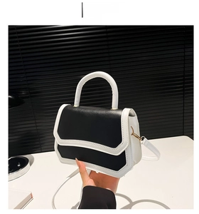 Detail of a minimalist black and white color block crossbody bag with gold hardware