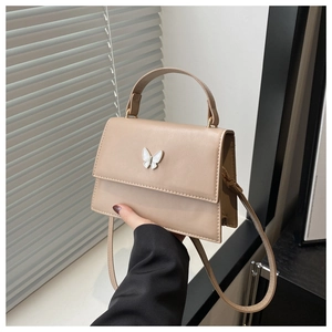 Detail of beige flap handbag featuring an elegant white enamel butterfly metal ornament