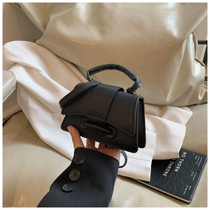 Detail of black lychee grain mini handbag with metal ring clasp held by a model