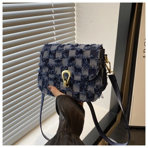 Détail du sac bandoulière en denim avec boucle dorée et finitions à bords effilochés