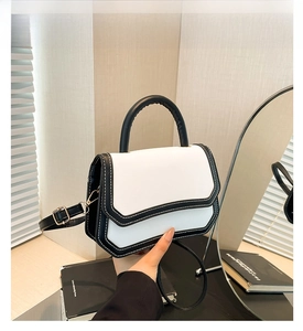 Detail of white leather bag with black contrast stitching and elegant top handle