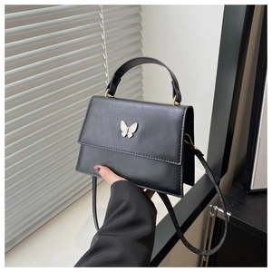 Close-up of black square handbag featuring a white butterfly metallic ornament and top handle
