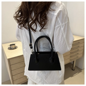 Minimalist black pebbled leather satchel with top handles shown on model in modern setting