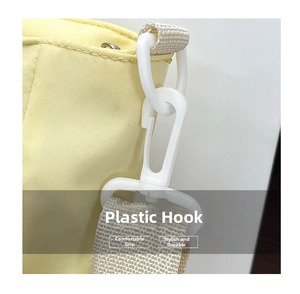 Detail of a white plastic hook connected to a beige woven strap on a light yellow tote bag