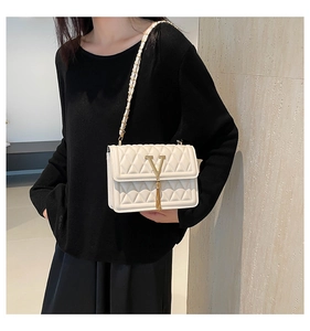 Detail of white quilted crossbody bag with gold V hardware, tassels and chain strap