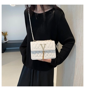 Detail showing white quilted chain bag with gold V logo and tassel ornament