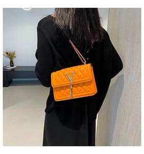 Detail of bright orange quilted crossbody bag with silver V-logo and metal tassel