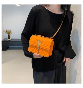 Detail of bright orange quilted crossbody bag featuring gold V logo and tassel