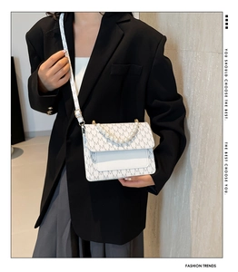 Detail of crossbody bag with pearl handle and M-letter print on cream texture