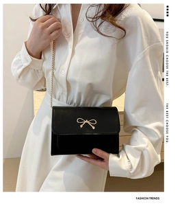 Close-up of black square flap bag with gold bow detail and metallic chain strap