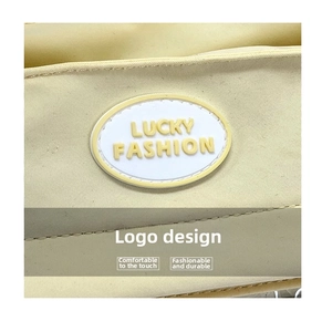 Detail of LUCKY FASHION rubber logo patch on a yellow canvas shoulder bag with stitching