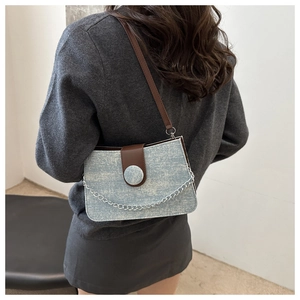 Détail du sac bandoulière en denim bleu clair avec garniture en cuir marron et chaîne