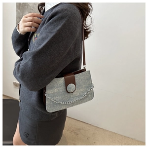 Detail of grey fabric tote with brown leather flap and silver chain on female model