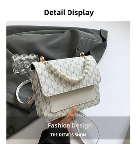 Detail of white square bag with pearl handle and repeating letter pattern finish
