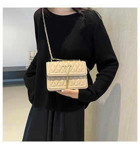 Detailed shot of beige quilted crossbody bag with metal V-buckle and tassel chain strap