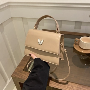 Elegant beige crossbody bag with butterfly buckle and top handle in a warm indoor setting