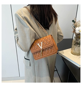 Detail of caramel quilted leather bag with gold V-buckle and elegant chain strap