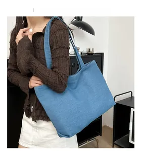 Detailed close-up of blue denim tote bag texture and wide shoulder strap on model