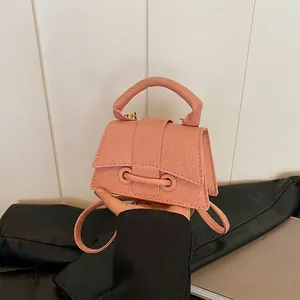 Pink lychee texture crossbody bag with top handle and metal buckle shown in hand
