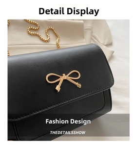 Detail view of black crossbody bag with gold bow clasp and metallic chain strap