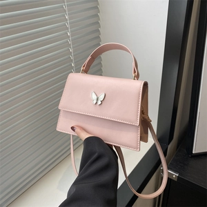 Elegant pink square handbag with butterfly charm and handle, displayed by window side