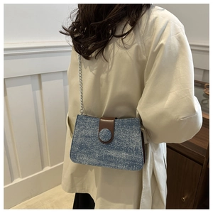 Detail of blue denim chain tote with brown leather buckle strap and silver chain