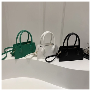 Minimalist square handbags in green, white, and black colors displayed on a podium