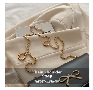 Detail of elegant gold box chain strap and decorative metal bow on a black leather bag