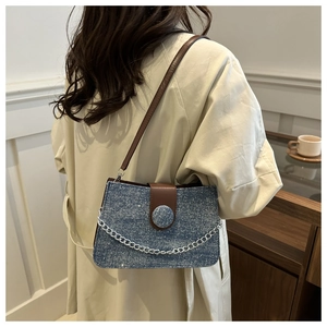 Detailed shot of a blue denim shoulder bag with brown leather accents and silver chain